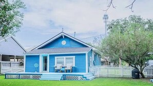 Une maison bleue avec un porche, une cour clôturée et un arbre.
