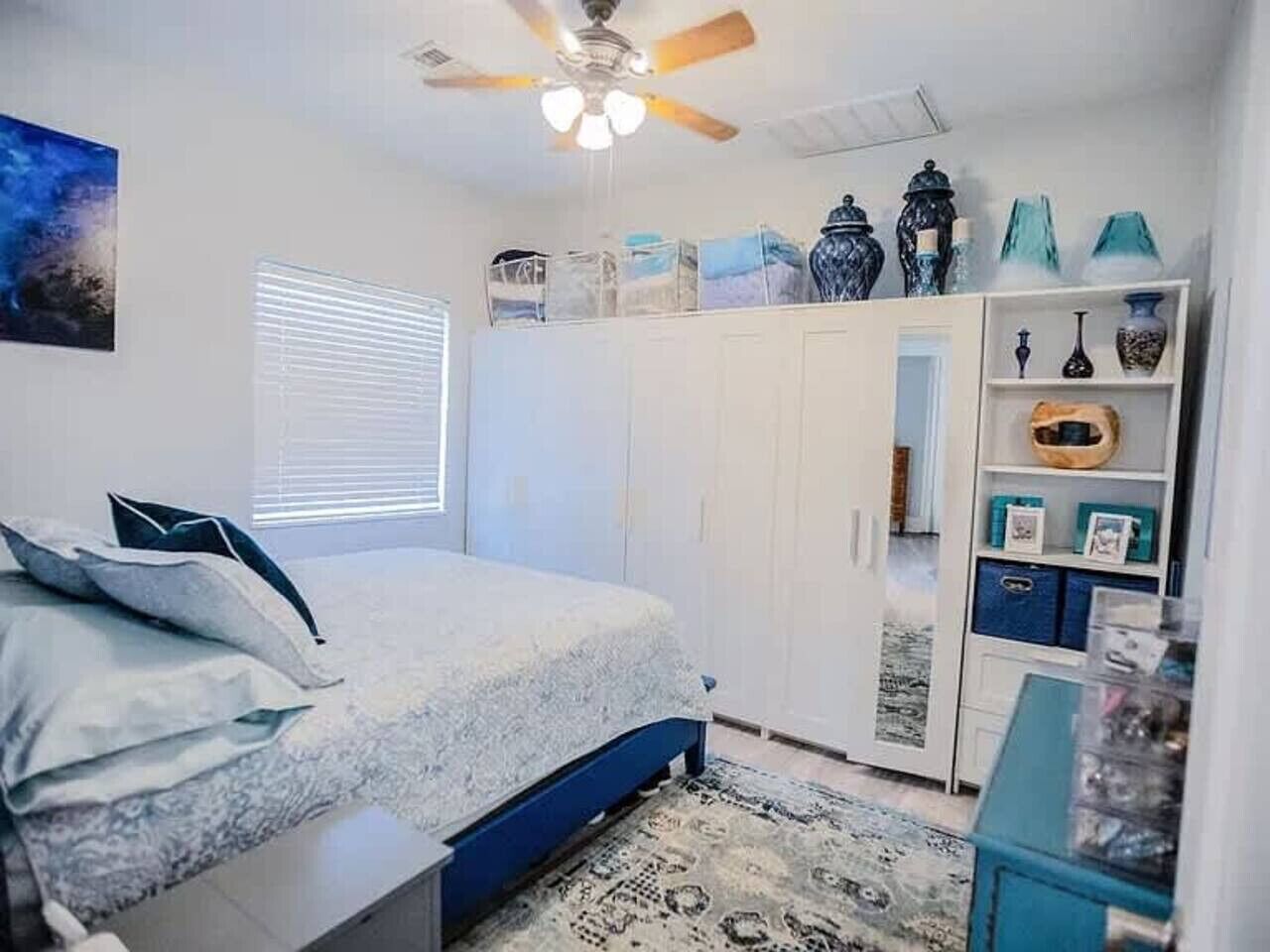 Ein Schlafzimmer mit Bett, Kleiderschrank, Deckenventilator und einem Fenster mit Jalousien.