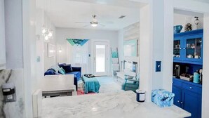 Une cuisine moderne avec un plan de travail en marbre blanc, un meuble bleu et un ventilateur de plafond.