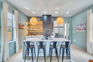 Una cocina moderna con una isla central, taburetes negros tipo barra, iluminación colgante y un salpicadero con diseño.