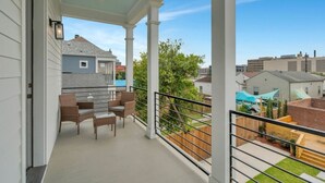 Un balcón cubierto con zona de estar, columnas blancas y vista a casas vecinas.