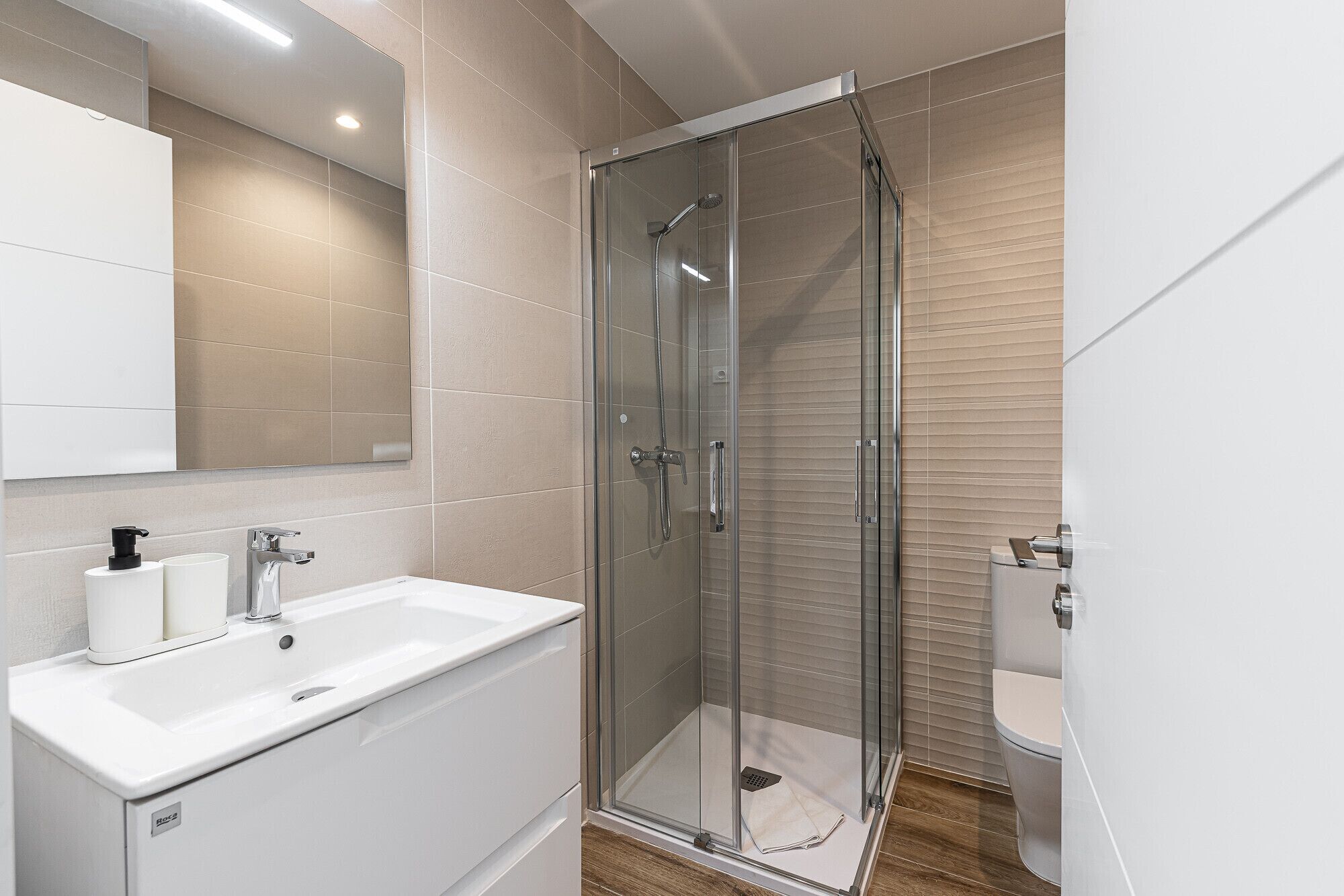 Un baño moderno con ducha de vidrio, lavamanos blanco y retrete.