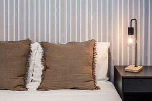 A bed with two pillows, a bedside table with a lamp, and a striped wallpaper background.