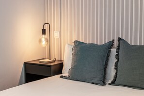 A neatly made bed with two pillows, a bedside table with a lamp, and a striped wall in the background.