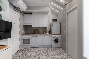 A compact kitchen with white cabinets, a microwave, a built-in oven, a washing machine, and a flat-screen TV.
