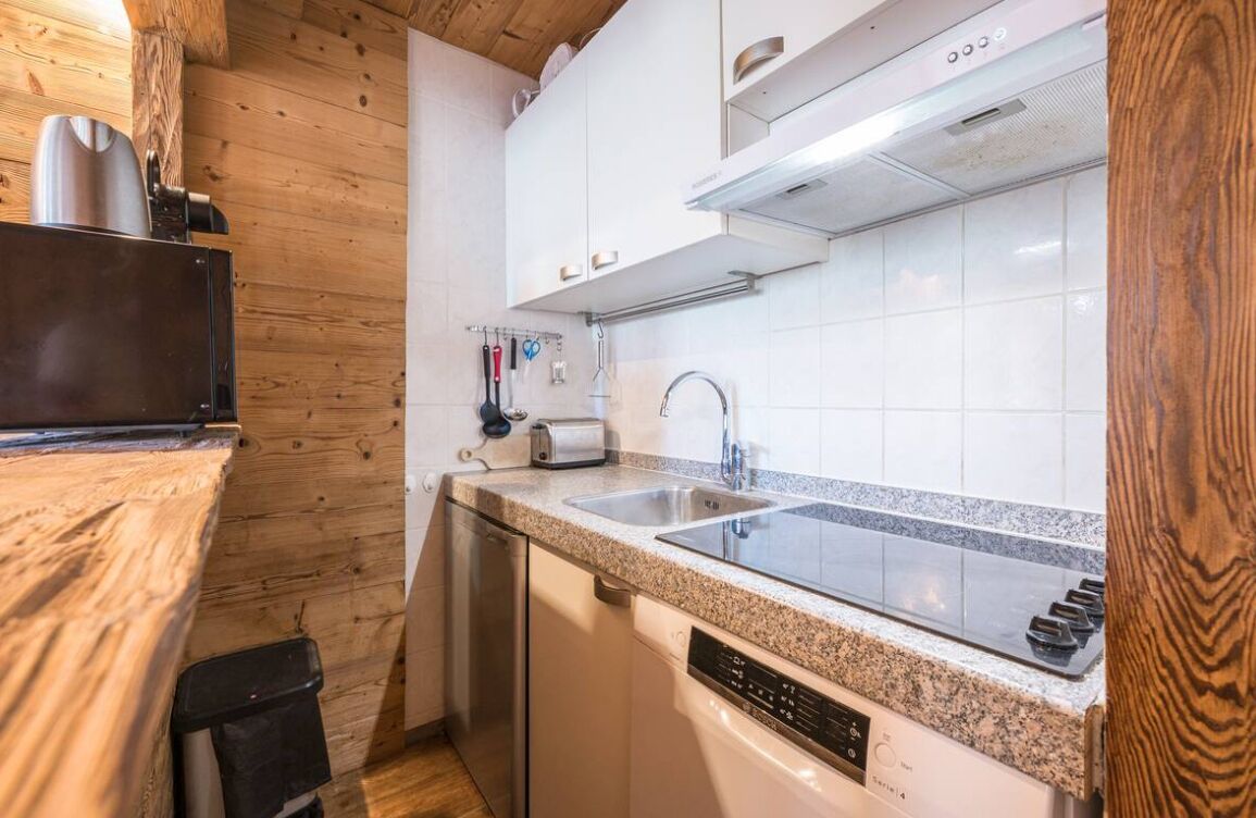 A compact kitchen with granite countertops, stainless steel appliances, and wooden paneling.