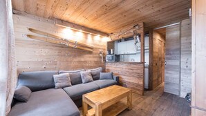 Een gezellig interieur van een blokhut met een houten plafond, een grijze bank, een houten salontafel en een keuken met kastjes en een magnetron.