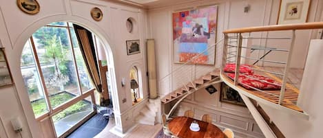 A room with a dining area, a staircase, and a large window.