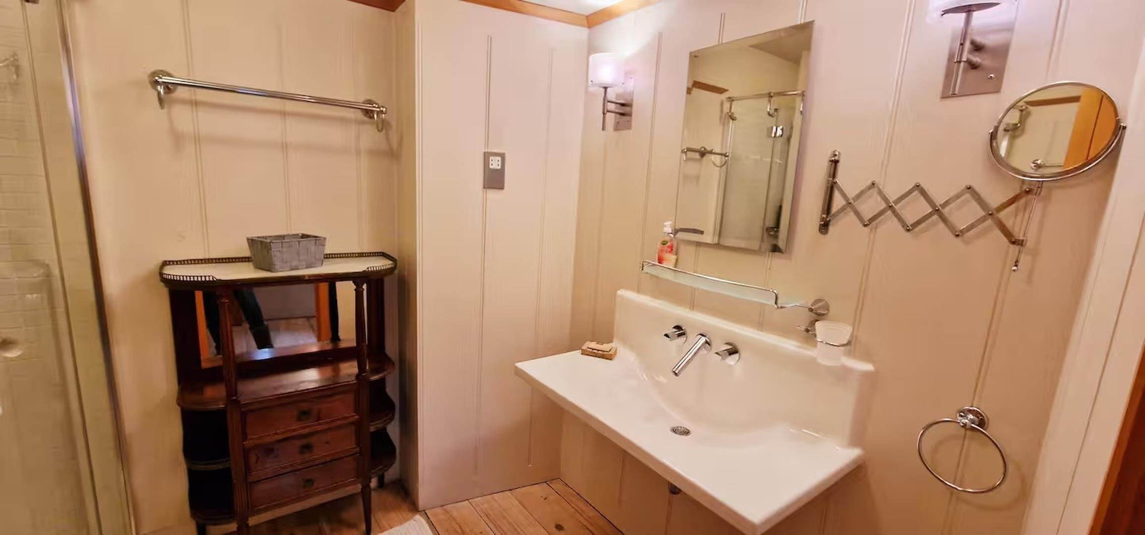 Un baño con tocador de madera, lavamanos, espejo y zona de ducha.