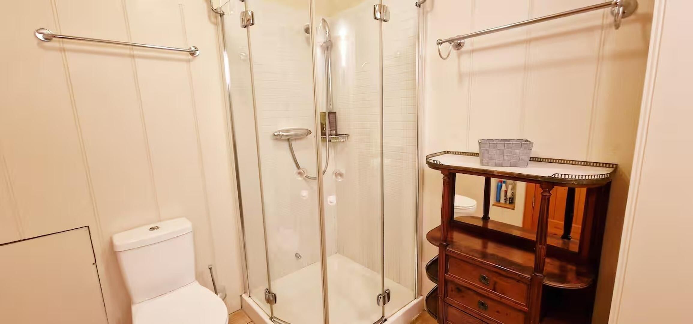A bathroom with a glass-enclosed shower, a wooden vanity, and a white toilet.
