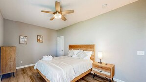 Un dormitorio con una cama de madera, una mesita de noche, un ventilador de techo y una puerta.