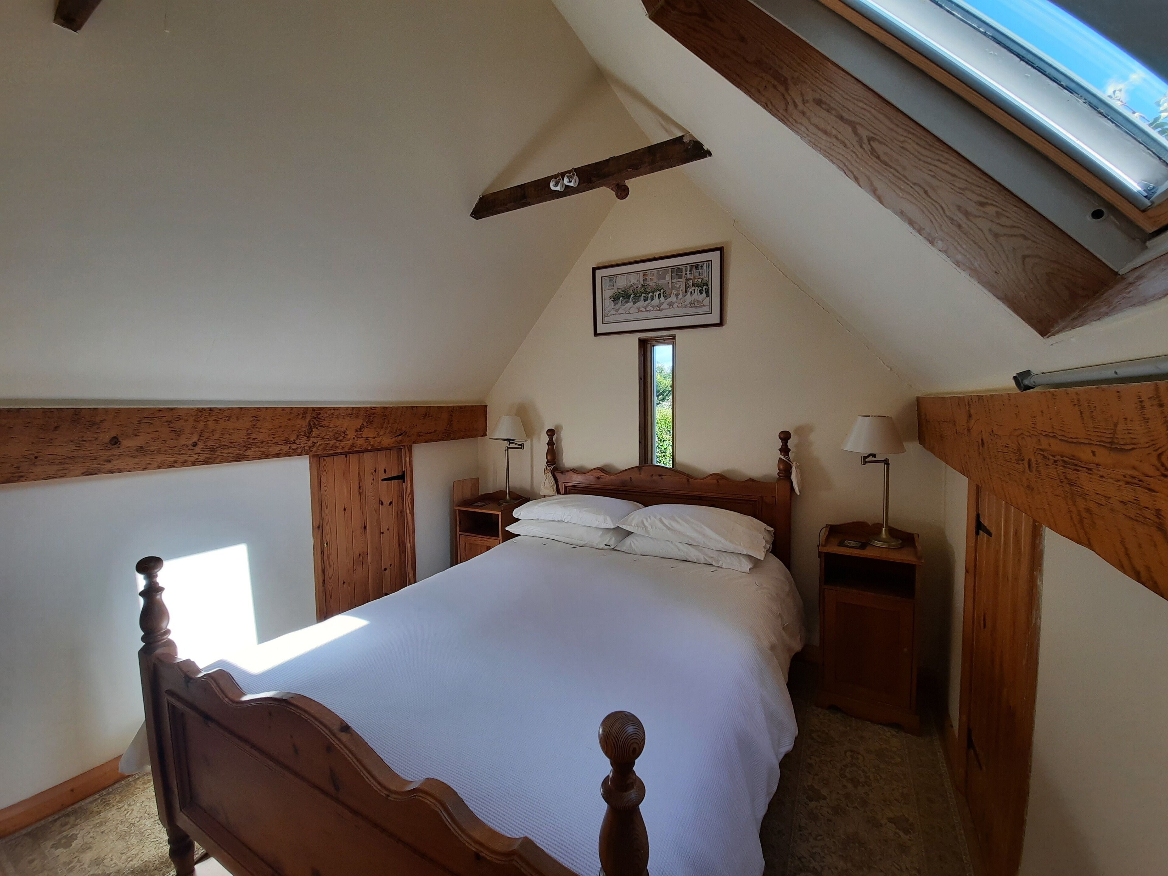 Una camera da letto con un letto di legno, un comodino, una lampada, un armadio e un lucernario.