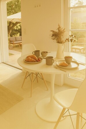 A dining area with a round table, white chairs, and a vase with dried flowers.