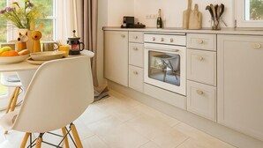 Een keuken met een eethoek, voorzien van een fornuis, oven en een plank met servies.