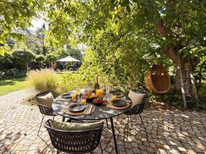 An outdoor dining area with a table set for two, surrounded by greenery and a cobblestone path.