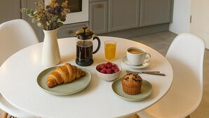 Een moderne keuken met grijze kastjes, een wit aanrecht en een raam. Er staat een eettafel met borden eten, een koffiepot en een vaas met bloemen.