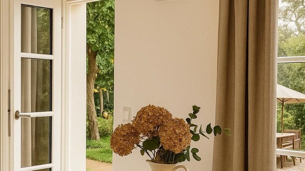 Een ronde eettafel met witte stoelen, een witte karaf, een fruitschaal, een bord met toast en een kop koffie.