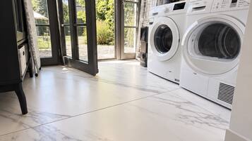 A laundry room with two front-loading washing machines, a large window with a view of greenery, and a marble floor.