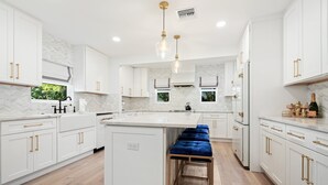 A modern kitchen with white cabinetry, a central island, and a blue bench.