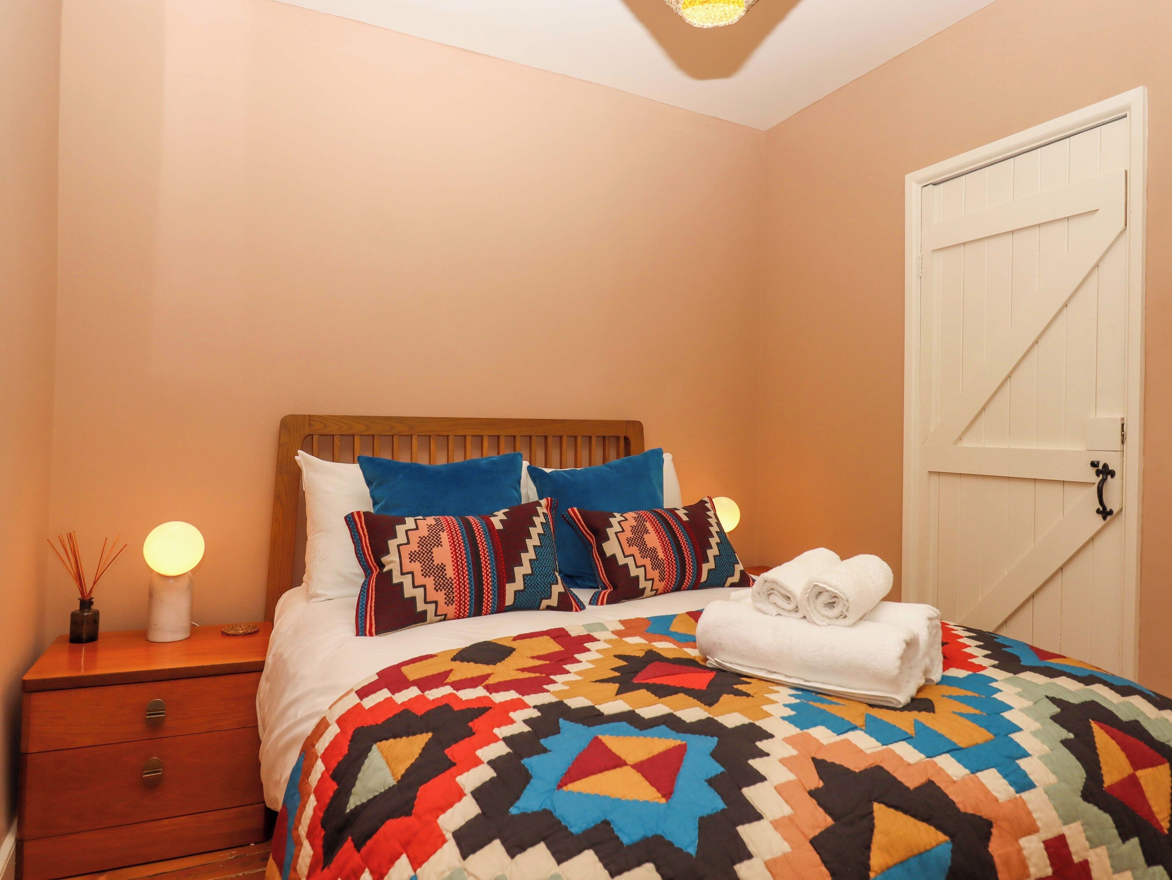 A bedroom with a wooden headboard, a colorful quilt, and a white door with a black handle.