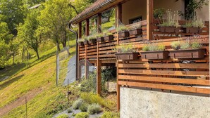 Un balcón de madera con plantas en macetas, un muro de concreto y un paisaje con colinas al fondo.