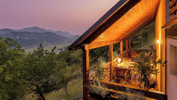 Terraza de madera con zona de comedor y vista a un paisaje montañoso.