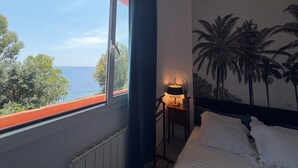 Un dormitorio con vista al mar, una cama, una mesita de noche con lámpara y un mural de palmeras.