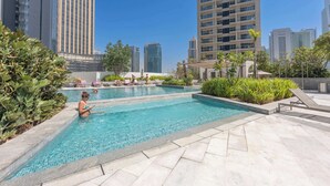 A swimming pool with lounge chairs and greenery, surrounded by tall buildings. - StayShort - Spacious Marina Stay for 6 with Canal Views (Dubai Marina)