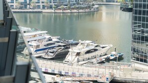 A marina with several yachts docked, surrounded by modern buildings and palm trees. - StayShort - Spacious Marina Stay for 6 with Canal Views (Dubai Marina)