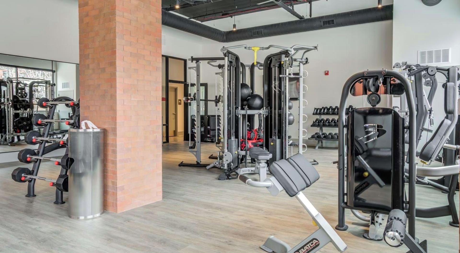 Un gimnasio con diversos equipos de ejercicio, que incluyen máquinas de pesas, pesas libres y máquinas de cardio.
