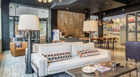 A modern hotel lobby with a sofa, coffee table, and dining area.