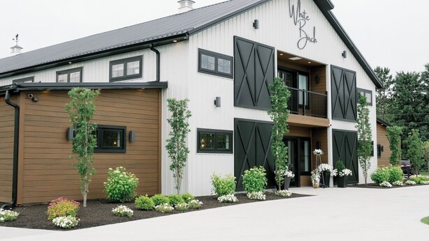 A two-story building with a white exterior and black accents, featuring a large garage door and a balcony. - Walk to Clark Lake + Beach Bar, Firepit, Porch, Sleeps 8 (Clarklake)