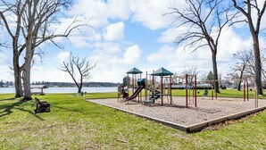 A playground with slides and climbing structures, surrounded by trees and a bench. - Walk to Clark Lake + Beach Bar, Firepit, Porch, Sleeps 8 (Clarklake)