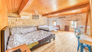 Une chambre avec deux lits, des murs en pierre, des poutres en bois au plafond et une table avec des chaises.