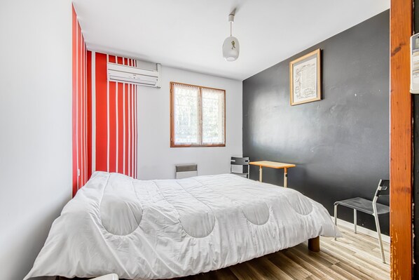 Un dormitorio con cama, escritorio, silla, ventana y aire acondicionado.