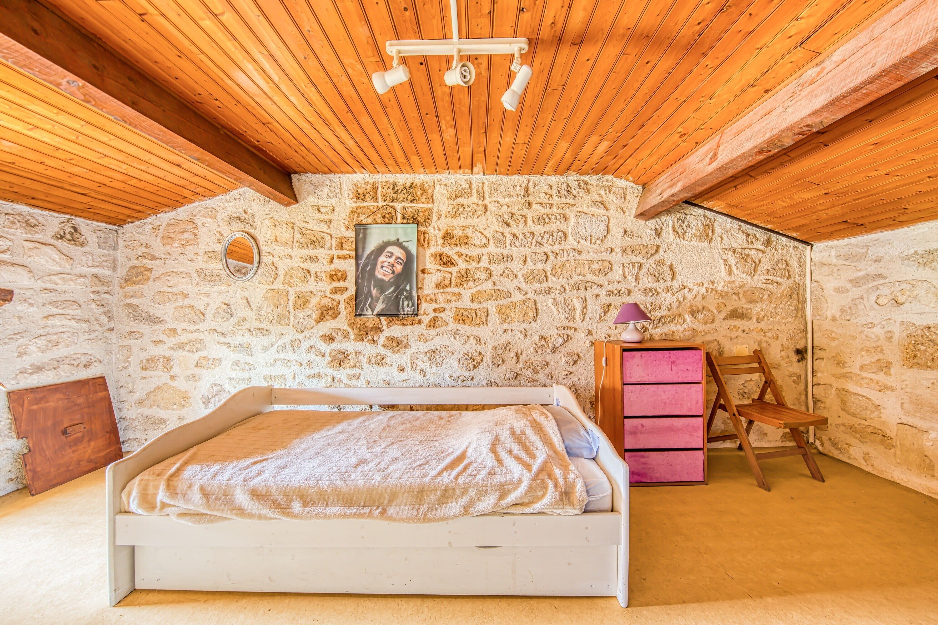 Ein Schlafzimmer mit einer Steinwand, einem Bett, einer Holzbalkendecke und einem kleinen Holzstuhl.