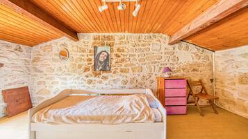 Ein Schlafzimmer mit einer Steinwand, einem Bett, einer Holzbalkendecke und einem kleinen Holzstuhl.