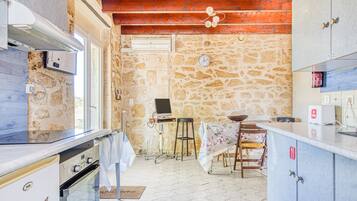 Une cuisine avec des murs en pierre, des poutres en bois au plafond, une table à manger avec des chaises et un petit téléviseur.