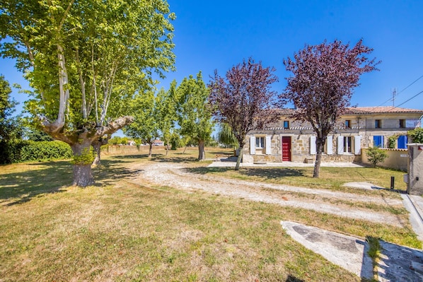 Une cour bordée d’arbres, un bâtiment avec une porte rouge et un ciel bleu azur.