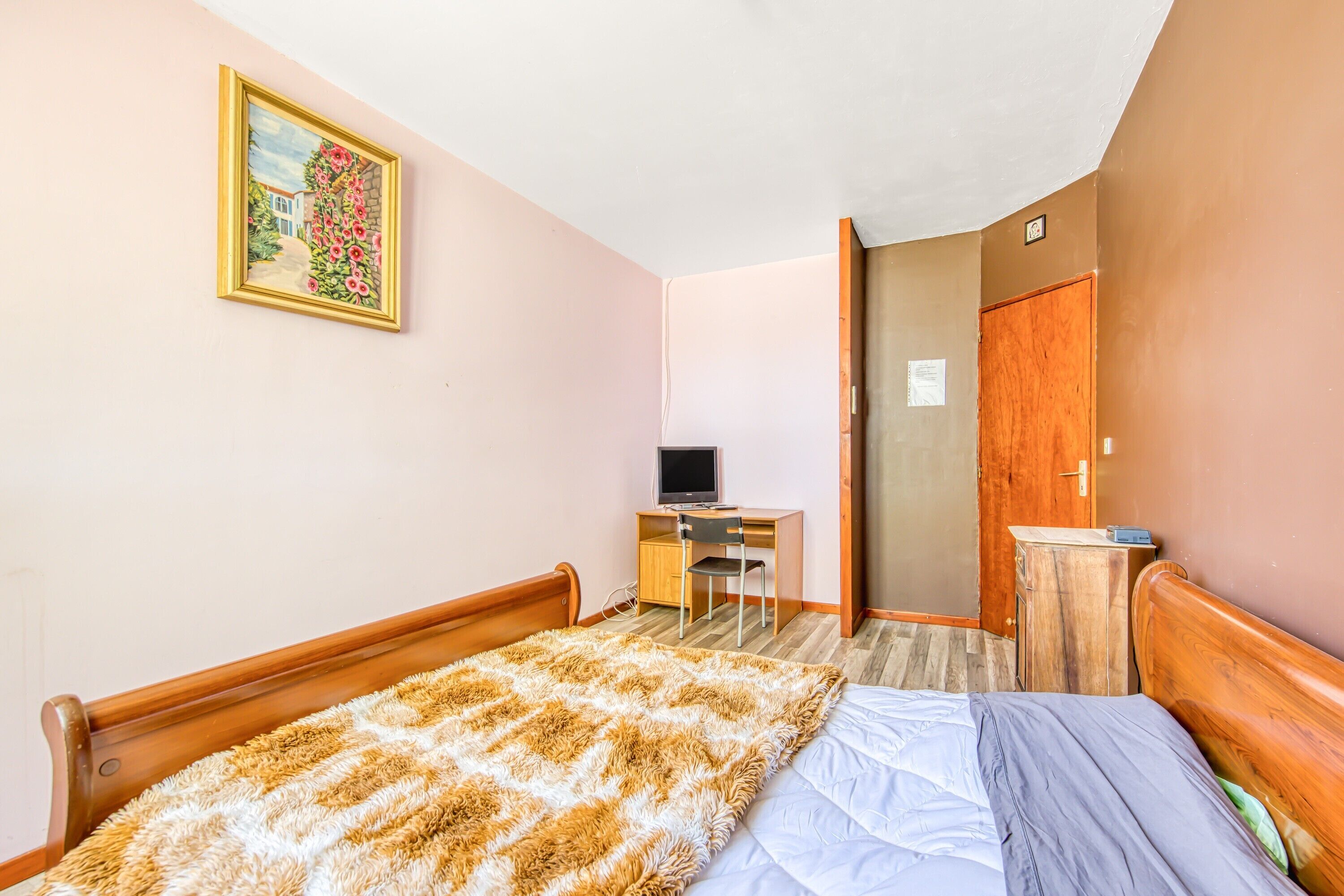 Une chambre à coucher avec un lit, un bureau avec un ordinateur, une chaise et une armoire en bois.