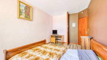 Une chambre à coucher avec un lit, un bureau avec un ordinateur, une chaise et une armoire en bois.