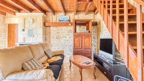 Un salon chaleureux avec un canapé, un meuble TV en bois, un mur en pierre et un escalier.