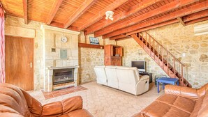 Un intérieur rustique avec un mur en pierre, des poutres en bois, une cheminée, des canapés en cuir et un escalier.
