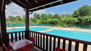 A covered outdoor area with a pool, red chairs, and a table. - Bungalow Privas (AZALÉE (Unknown)