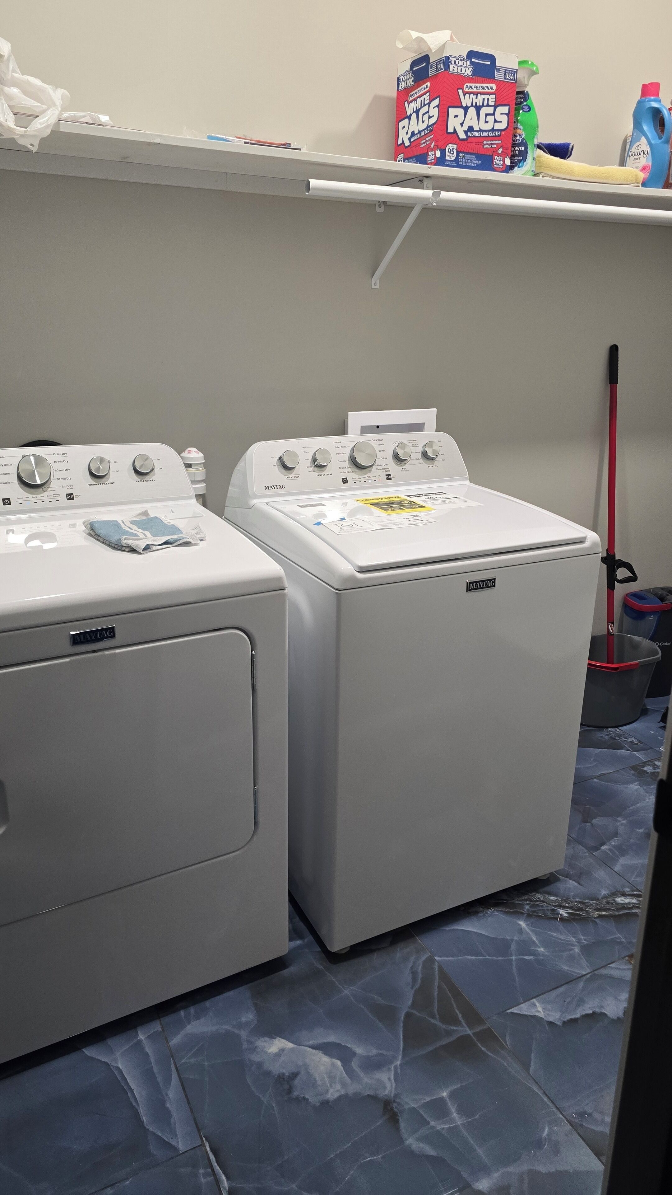 Dos lavadoras Maytag de carga frontal y un estante con productos de limpieza.