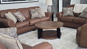 Un salon moderne avec des canapés en cuir marron, une table basse ronde en bois et des coussins décoratifs à motifs.