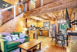 Interior de uma cabana de madeira com sala de estar, cozinha e espaço para refeições.