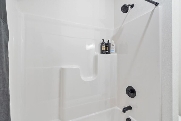 A white bathtub with a showerhead, a faucet, and a shelf with toiletries.