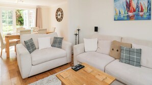A modern living room with two white sofas, a wooden coffee table, and a dining area with a table and chairs. - Lorien (Cheltenham)