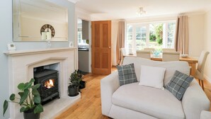 A living room with a fireplace, a sofa, and a dining area with a view of the garden. - Lorien (Cheltenham)